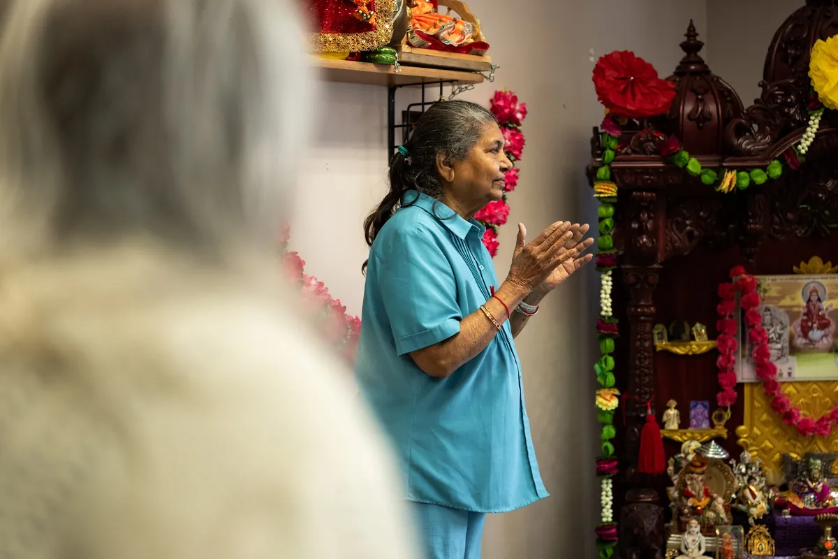 Resident with hands folded in prayer beside the decorated home shrine